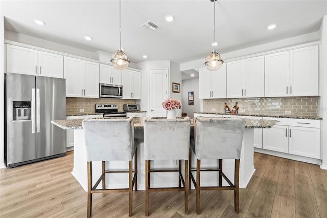 kitchen with white cabinetry, stainless steel appliances, pendant lighting, a kitchen island with sink, and light wood-type flooring