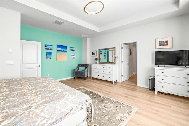 bedroom with light hardwood / wood-style floors and a raised ceiling