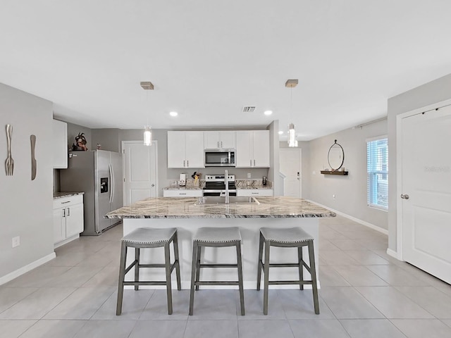 kitchen with a center island with sink, white cabinets, pendant lighting, and appliances with stainless steel finishes