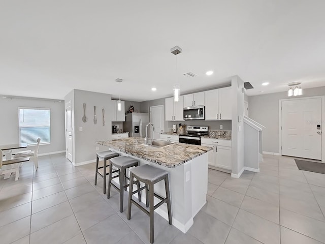 kitchen featuring a kitchen island with sink, sink, appliances with stainless steel finishes, light stone counters, and white cabinetry