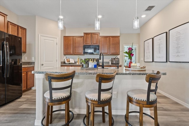 kitchen featuring hanging light fixtures, light hardwood / wood-style floors, a kitchen island with sink, and black appliances