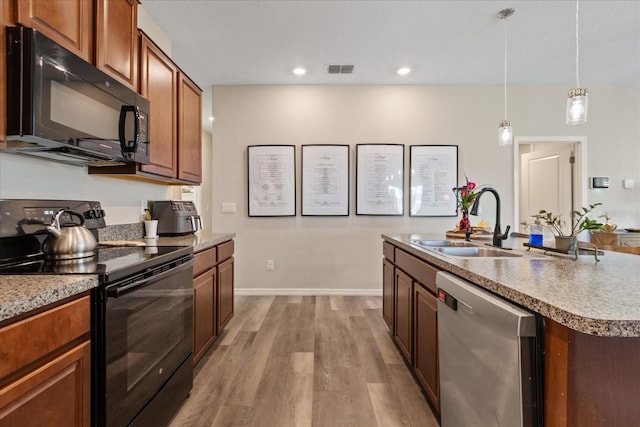 kitchen featuring black appliances, sink, hanging light fixtures, light hardwood / wood-style flooring, and an island with sink