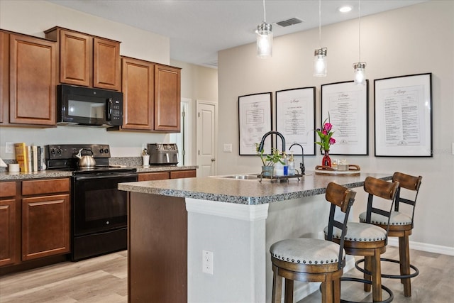 kitchen with a kitchen island with sink, sink, black appliances, light hardwood / wood-style floors, and a breakfast bar area