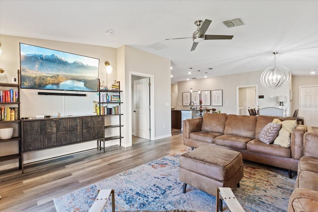 living room with ceiling fan with notable chandelier and hardwood / wood-style flooring