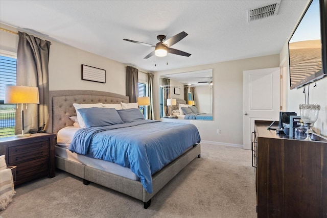 bedroom featuring multiple windows, ceiling fan, light carpet, and a textured ceiling