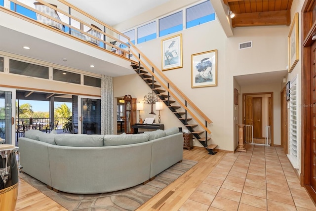 living room with beam ceiling, light wood-type flooring, a towering ceiling, and wood ceiling