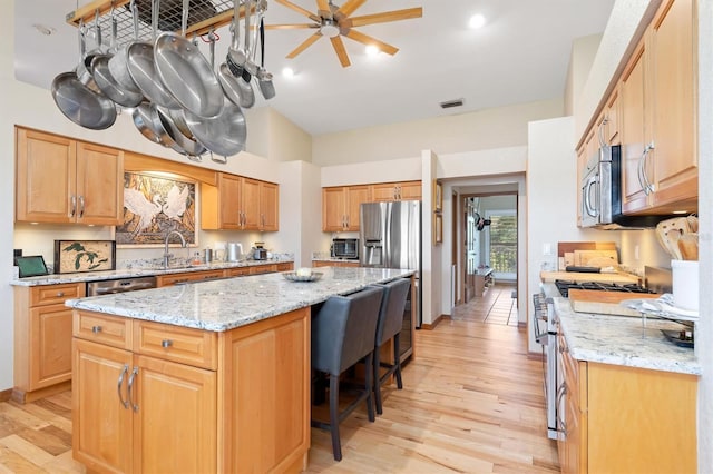 kitchen featuring a center island, ceiling fan, light stone countertops, light hardwood / wood-style floors, and stainless steel appliances