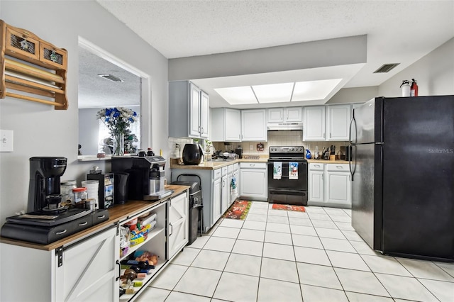 kitchen with light tile patterned flooring, a textured ceiling, decorative backsplash, white cabinets, and black appliances