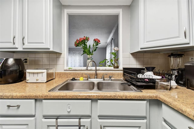 kitchen featuring white cabinets, backsplash, and sink