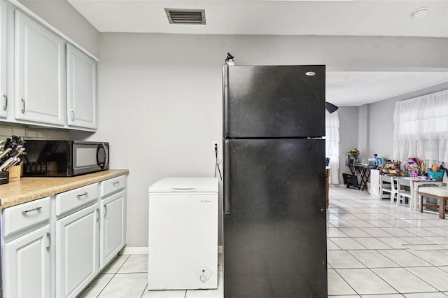 kitchen featuring decorative backsplash, light tile patterned floors, white cabinetry, and black appliances