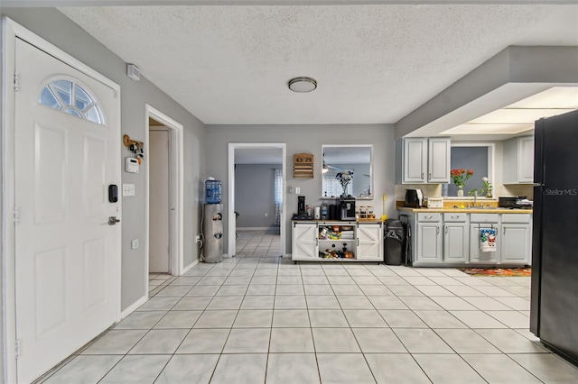 kitchen featuring sink, light tile patterned flooring, black fridge, and a textured ceiling