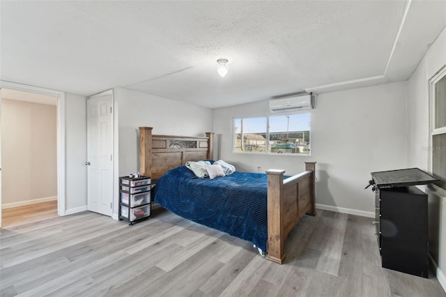 bedroom with a wall unit AC, a textured ceiling, and light wood-type flooring