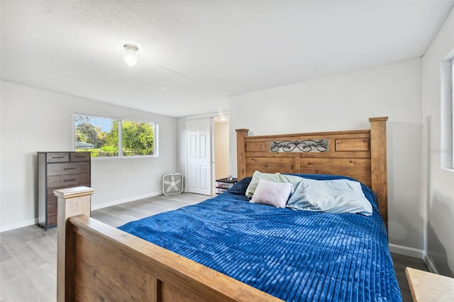 bedroom featuring a textured ceiling, light wood finished floors, and baseboards
