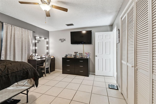 bedroom with a closet, baseboards, light tile patterned floors, a textured ceiling, and a ceiling fan