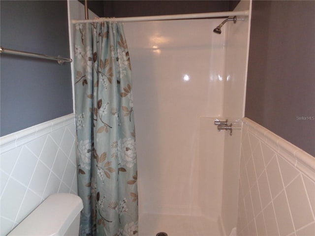 full bathroom with toilet, a shower with shower curtain, wainscoting, and tile walls