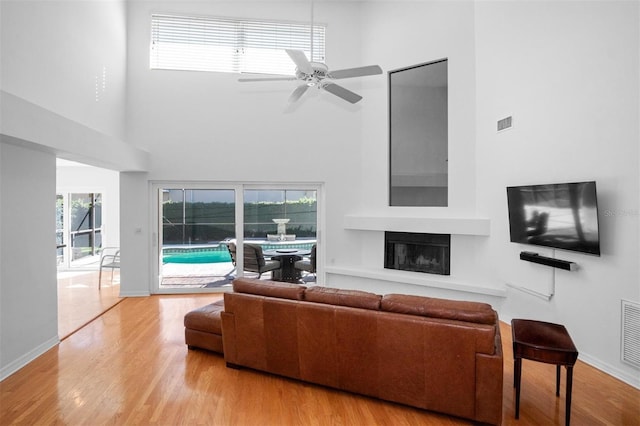 living room with a high ceiling, light wood-type flooring, and ceiling fan