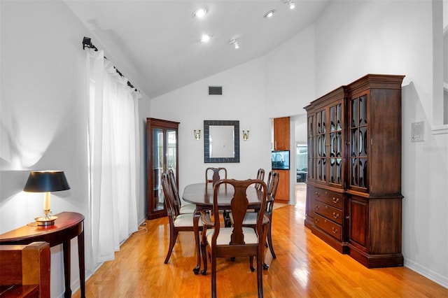 dining room with light hardwood / wood-style flooring and high vaulted ceiling