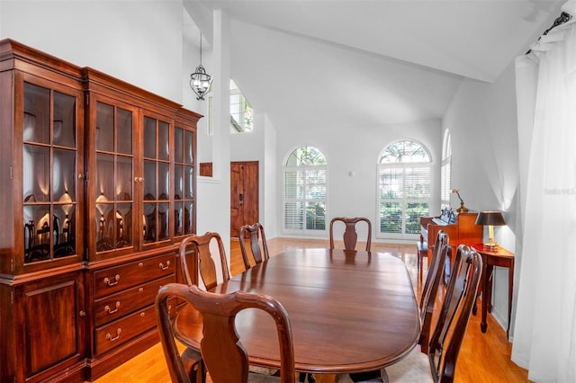 dining space featuring light wood-type flooring, high vaulted ceiling, and a notable chandelier