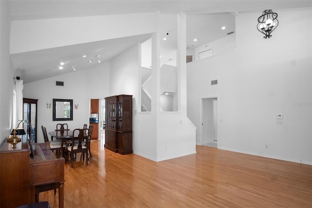 living room featuring high vaulted ceiling, light hardwood / wood-style floors, and an inviting chandelier