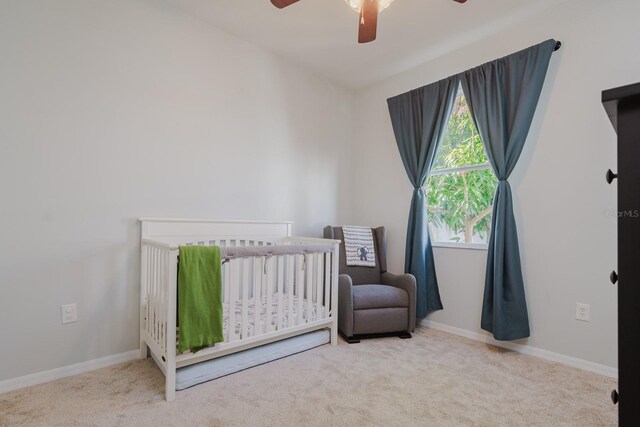 carpeted bedroom with ceiling fan and a nursery area