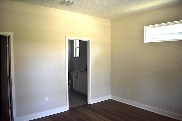 unfurnished room with baseboards, dark wood-style floors, a textured ceiling, and visible vents