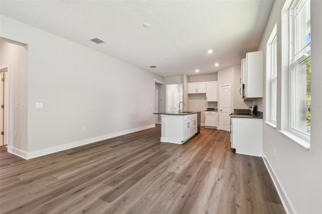 2735 36th Ave N, Saint Petersburg, FL 33713 - kitchen with dark countertops, a center island with sink, white cabinets, wood finished floors, and baseboards