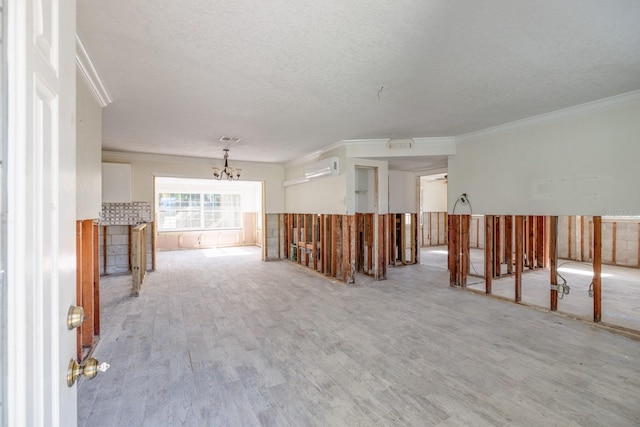 spare room featuring light wood-type flooring, a textured ceiling, ornamental molding, a wall mounted AC, and a chandelier