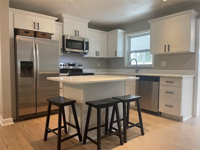 kitchen with white cabinets, light hardwood / wood-style floors, stainless steel appliances, and a textured ceiling