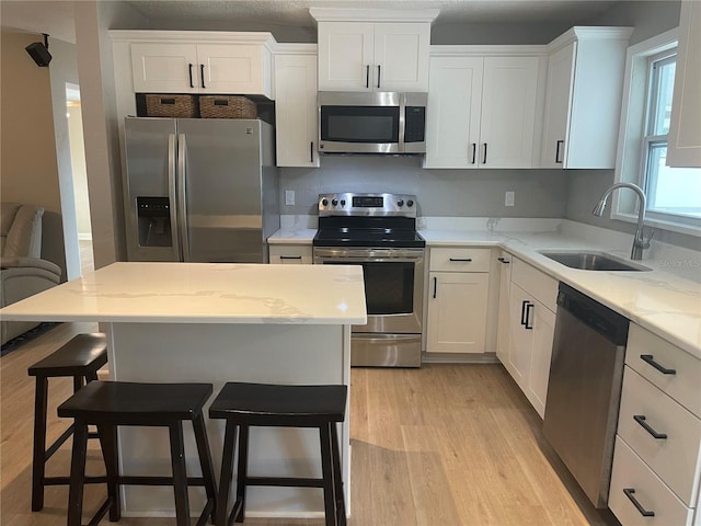 kitchen with stainless steel appliances, sink, light hardwood / wood-style flooring, white cabinets, and a center island