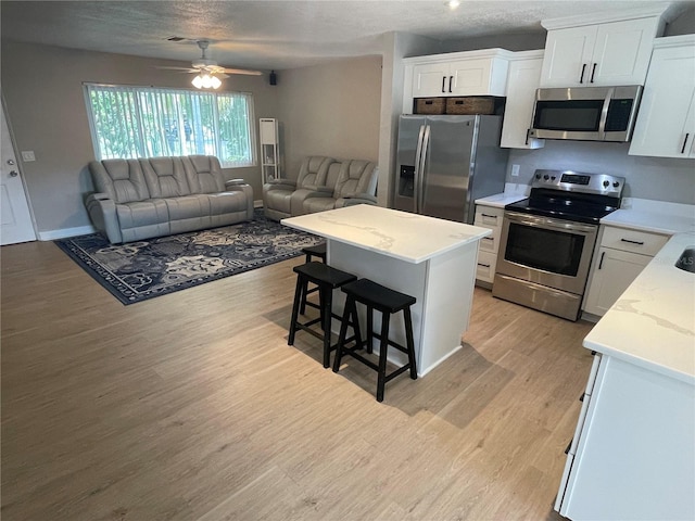 kitchen with a center island, white cabinets, light wood-type flooring, appliances with stainless steel finishes, and a kitchen bar