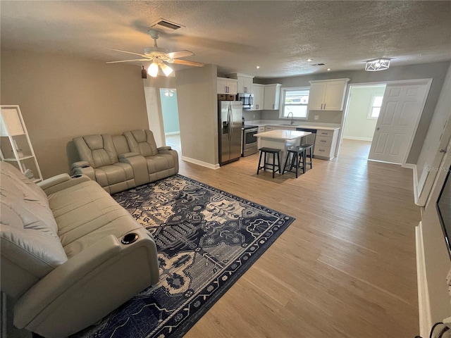 living room with a textured ceiling, light hardwood / wood-style floors, ceiling fan, and sink