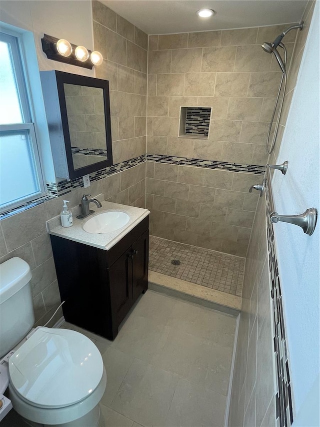 bathroom featuring vanity, toilet, a tile shower, and tile walls