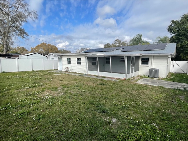 rear view of house with central air condition unit, a sunroom, a yard, and solar panels