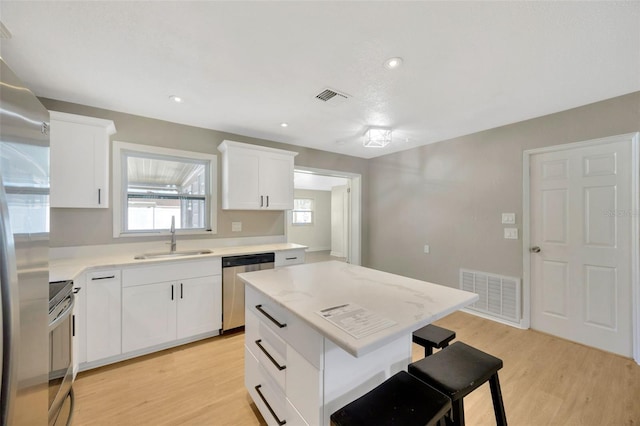 6598 26th St N, Saint Petersburg, FL 33702 - kitchen with sink, stainless steel appliances, white cabinets, a kitchen island, and light wood-type flooring