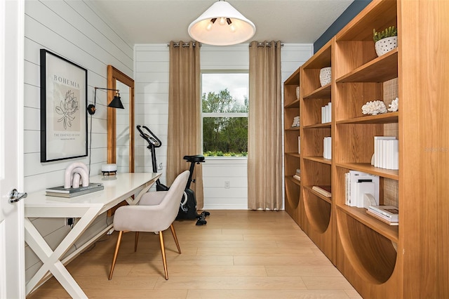 office area with light wood-type flooring and wood walls