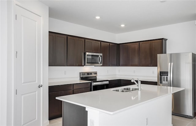 kitchen with light tile patterned floors, dark brown cabinets, stainless steel appliances, and a sink