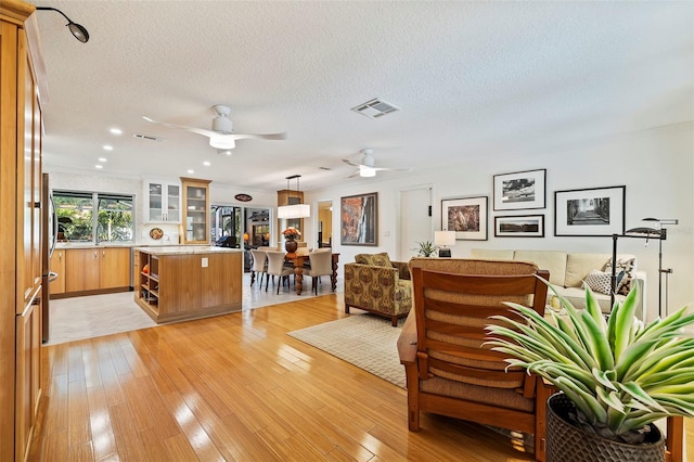 unfurnished living room featuring ceiling fan, light wood-type flooring, and a textured ceiling