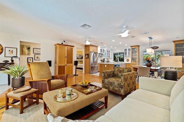 living room featuring ceiling fan, crown molding, light hardwood / wood-style floors, and a textured ceiling