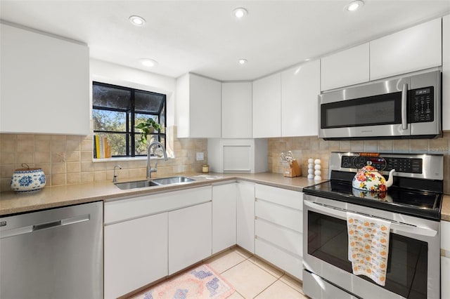 kitchen with backsplash, sink, light tile patterned floors, white cabinetry, and stainless steel appliances