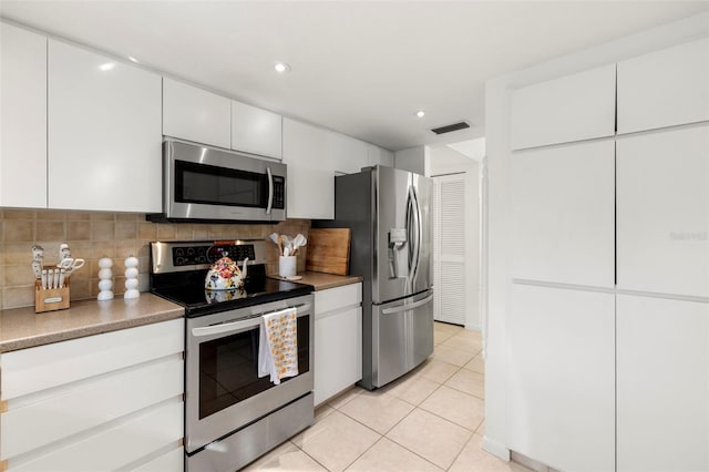 kitchen with tasteful backsplash, white cabinetry, light tile patterned floors, and appliances with stainless steel finishes