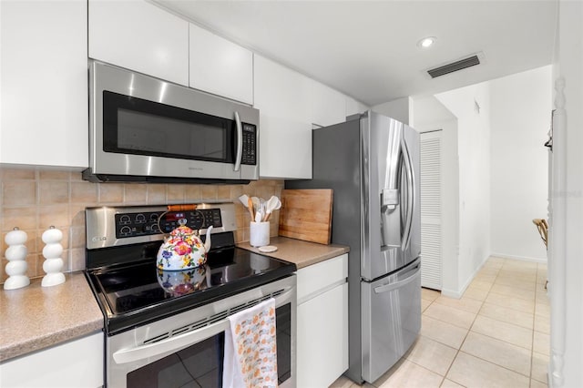 kitchen featuring decorative backsplash, white cabinetry, stainless steel appliances, and light tile patterned floors