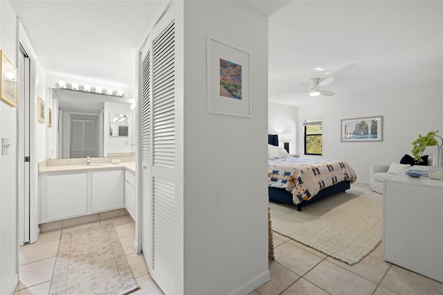 tiled bedroom with ensuite bath, ceiling fan, sink, and a textured ceiling