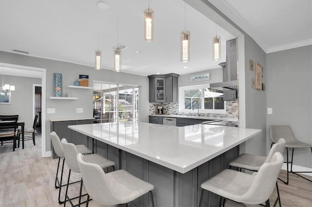 kitchen featuring decorative light fixtures, light hardwood / wood-style floors, gray cabinetry, and a breakfast bar area