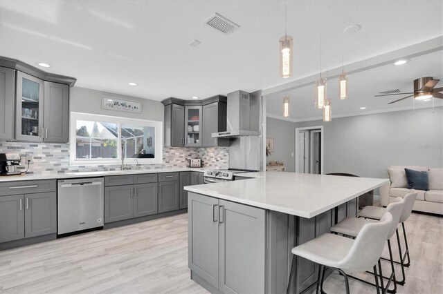 kitchen featuring gray cabinets, wall chimney range hood, and appliances with stainless steel finishes