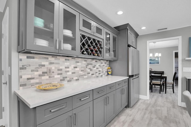 kitchen with pendant lighting, light hardwood / wood-style flooring, gray cabinets, tasteful backsplash, and a notable chandelier