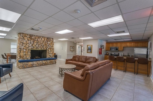 tiled living room with a stone fireplace and a drop ceiling