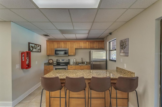 kitchen with kitchen peninsula, appliances with stainless steel finishes, a drop ceiling, sink, and a breakfast bar area