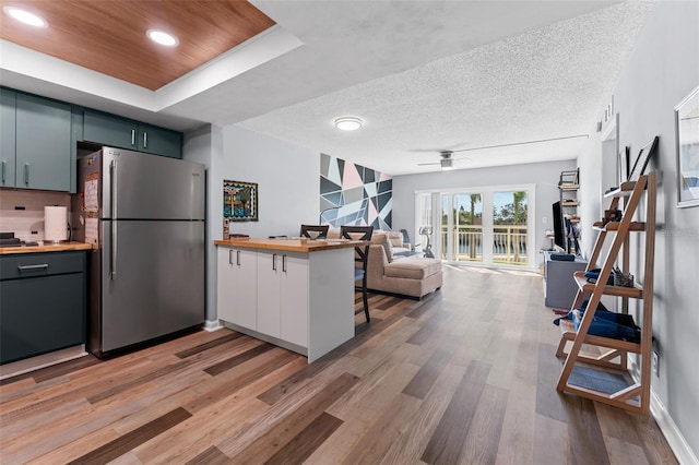 kitchen with butcher block counters, hardwood / wood-style flooring, kitchen peninsula, a breakfast bar area, and stainless steel refrigerator