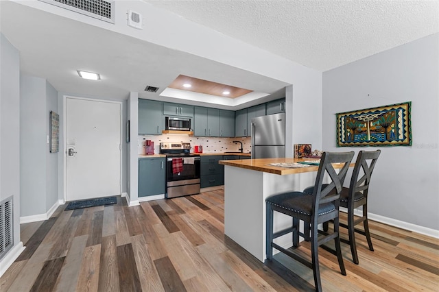 kitchen with wood counters, a raised ceiling, appliances with stainless steel finishes, light hardwood / wood-style floors, and a kitchen bar