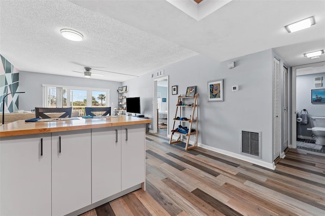 kitchen featuring butcher block counters, white cabinetry, ceiling fan, hardwood / wood-style floors, and a textured ceiling